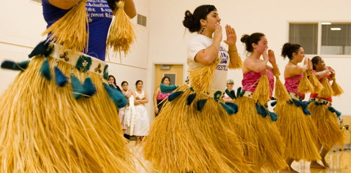 Several people dancing with long straw skirts.