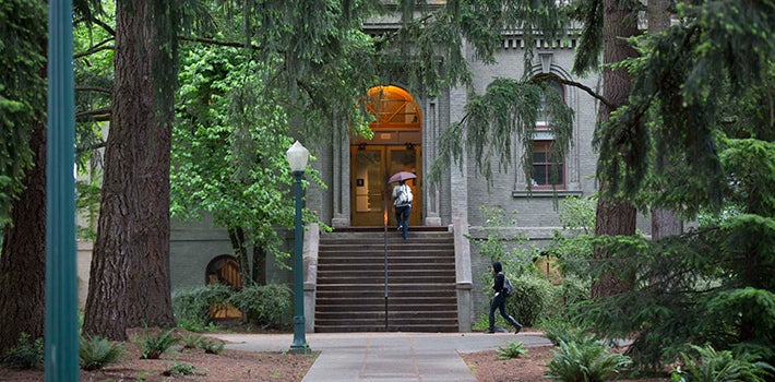 A student with an umbrella walks down the stairs leading out of Deady Hall.