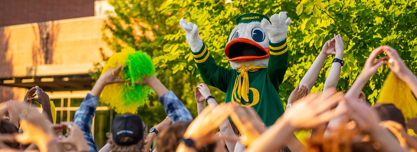 Oregon Duck mascot leading a cheer in front of a crowd of students