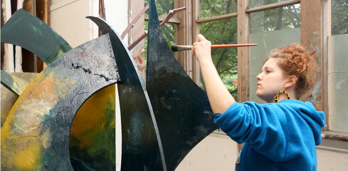 Painting a Sculpture A female student carefully paints a large, curved sculpture.