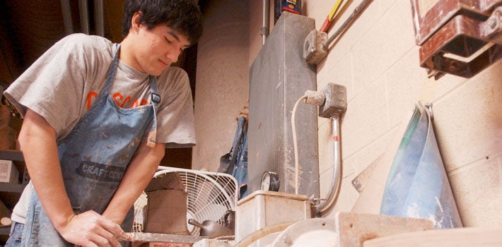 Student in Apron Working Clay A male student with a dirtied, blue apron works on some clay.