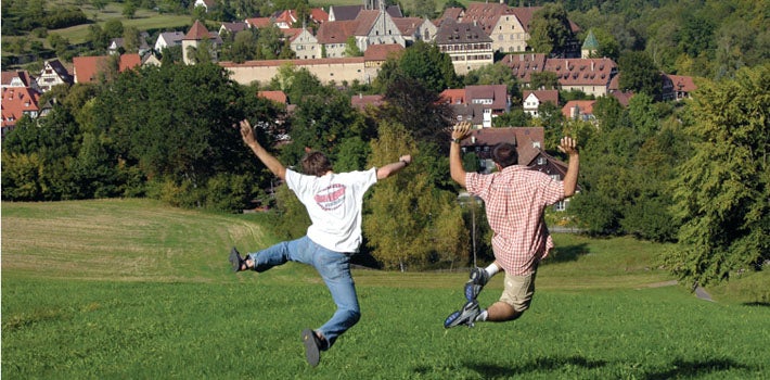 European Studies Two men leap from atop a hill, down the grassy slope.