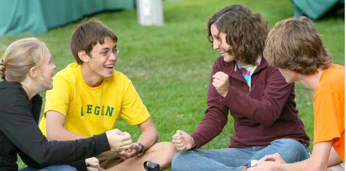 Students meeting, sitting, and laughing together on the grass.