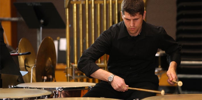 Playing the Timpani A male student in black pounds on the timpani.