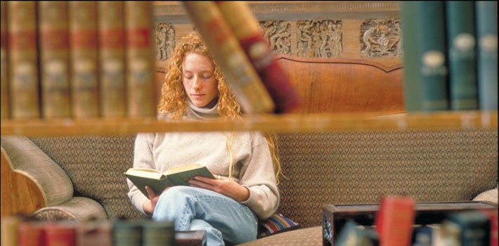 A student with long, red, curly hair reads quietly in the library.