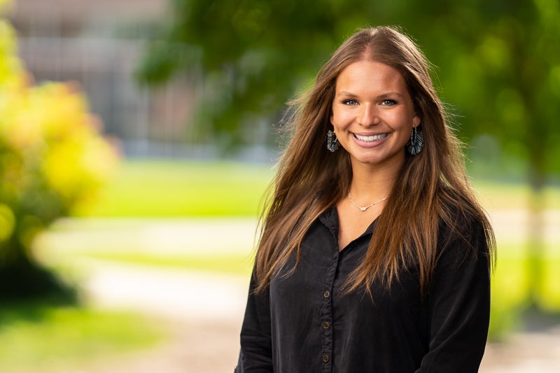 Katie Carter wearing a black shirt foreground, blurry trees and grass background