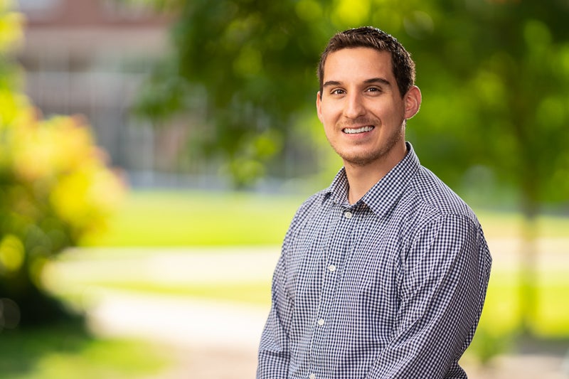 Lorenzo Wilcox wearing a blue patterned shirt foreground, blurry trees and grass background