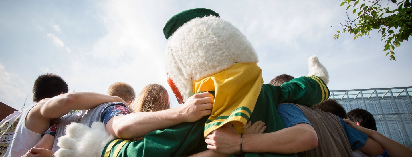 UO Duck mascot with a group of students grouped together for a photograph. Seen from behind and below.
