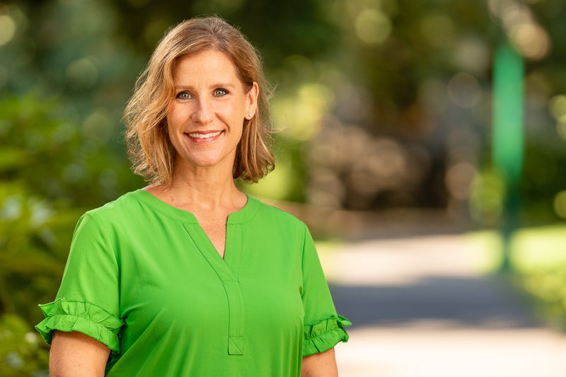 A woman looking at the camera in front of a forested pathway.