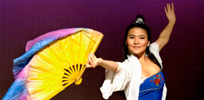 Woman in traditional blue and white Chinese dress happily dances with bright yellow, colorful fan.