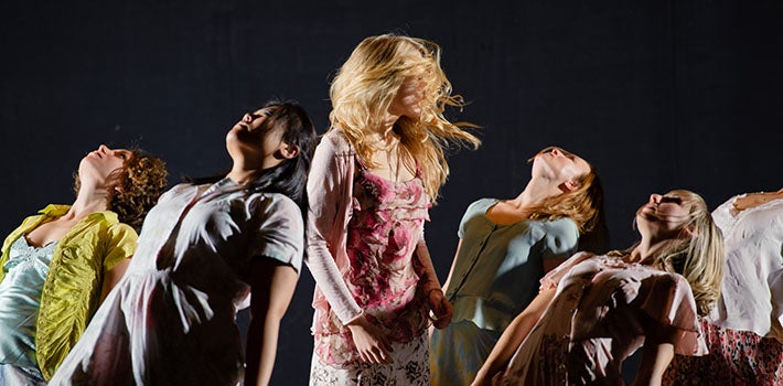 Five female students lean back, striking a pose as a blonde woman twirls in the center.