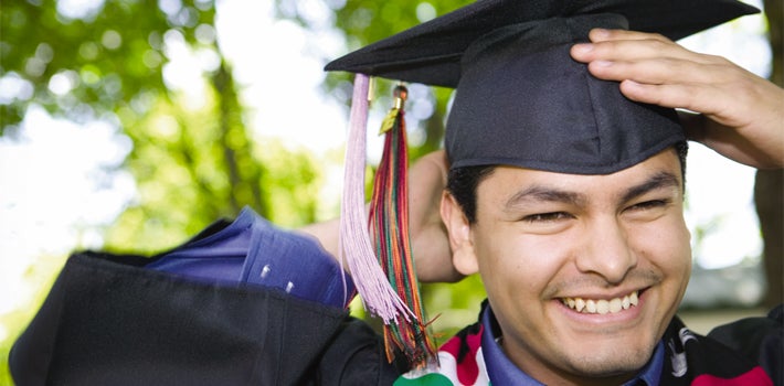 Male hispanic student smiling proudly in his graduation robe and cap.