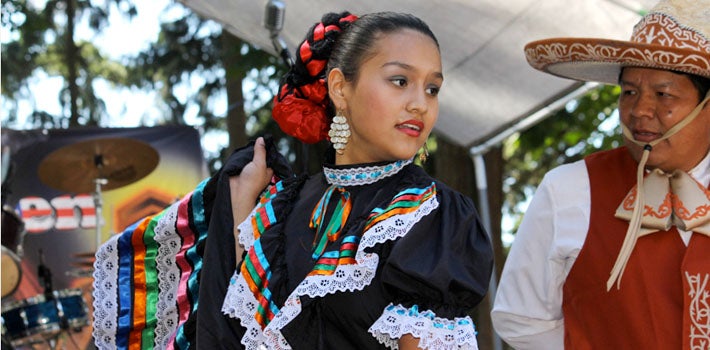 A hispanic woman and man, in festive garb, dance and perform.