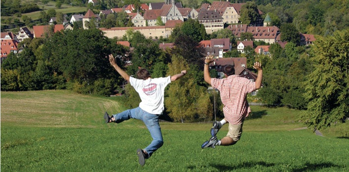 Two men leap from atop a hill, down the grassy slope.