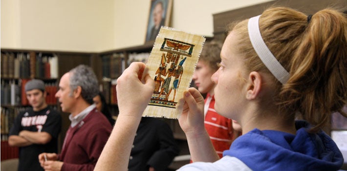 A student closely studies an old piece of art as her professor lectures.