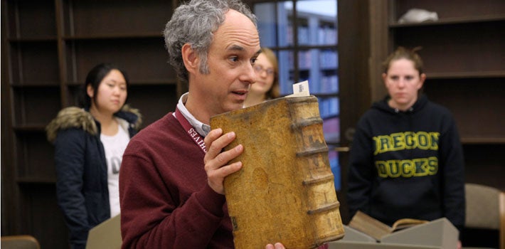 A professor displaying a huge tome of Latin writing.