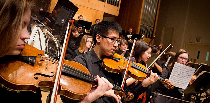 Violinists in an orchestra, performing on stage.