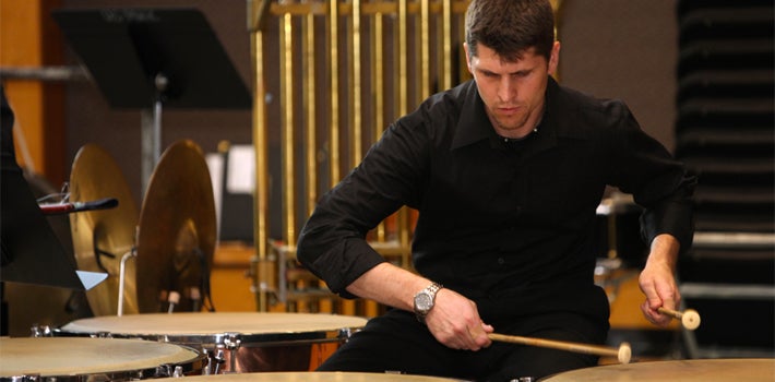 A male student in black pounds on the timpani.