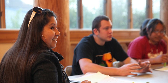 Three students having a conversation in the Many Nations Longhouse.