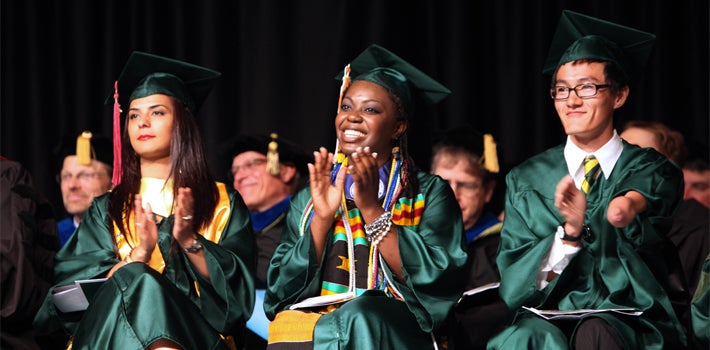 Three graduating students, of different race and gender, all smiling and applauding together.