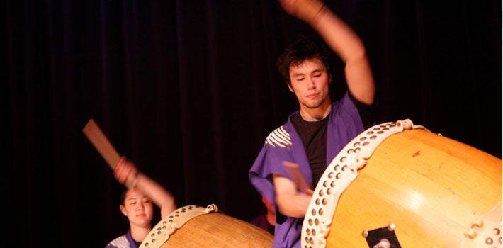 Two students playing large, traditional drums.